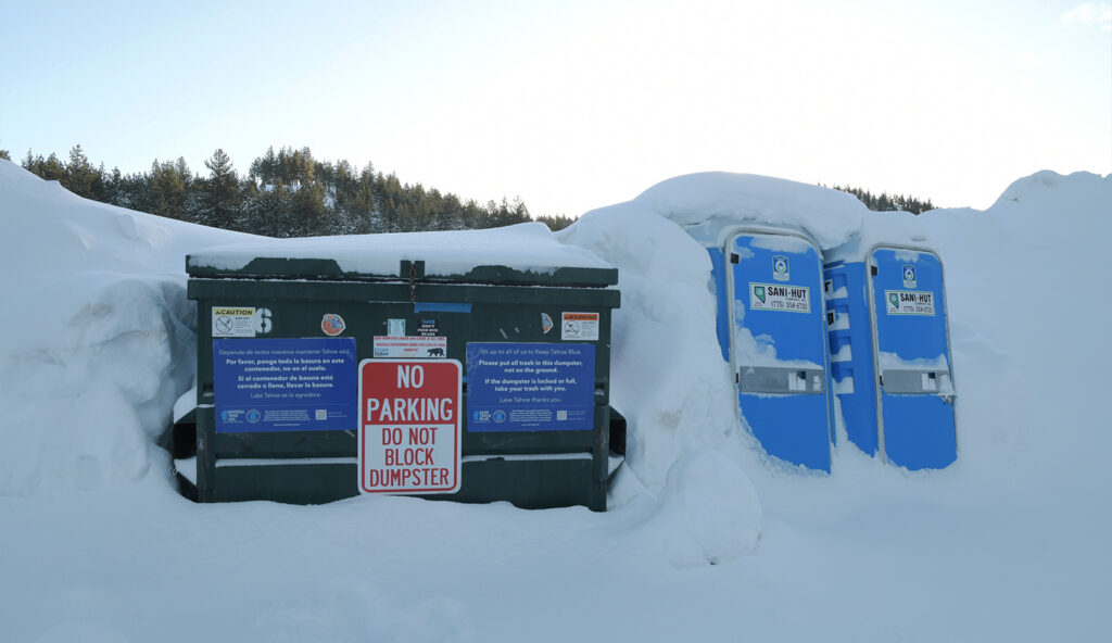 A dumpster and two portable toilets in the snow.