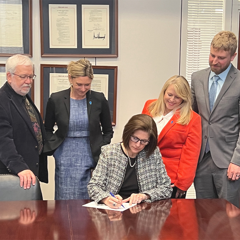 A group looks on as someone signs a bill